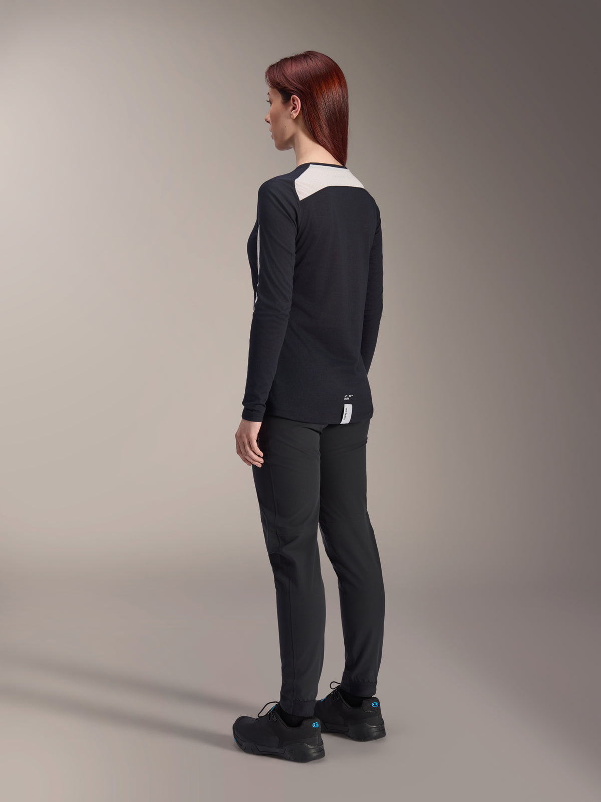 Vrouwelijke rijder in Alpinestars Stella A-Dura damesbroek en Stella A-Dura Elite jersey, zwart, achteraanzicht met witte mesh schouderpanelen op de jersey met lange mouwen, slim-fit technische broek, gecoördineerde mountainbike-uitrusting.