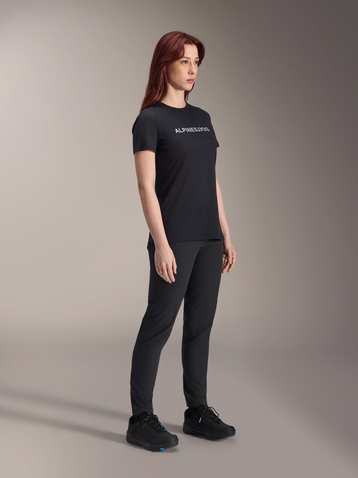 Alpinestars Stella A-Dura Dri Switch jersey, fietsshirt met korte mouwen, zwart met wit Alpinestars-logo, gedragen door vrouwelijk model met bijpassende zwarte broek en schoenen, veelzijdige uitrusting voor mountainbiken