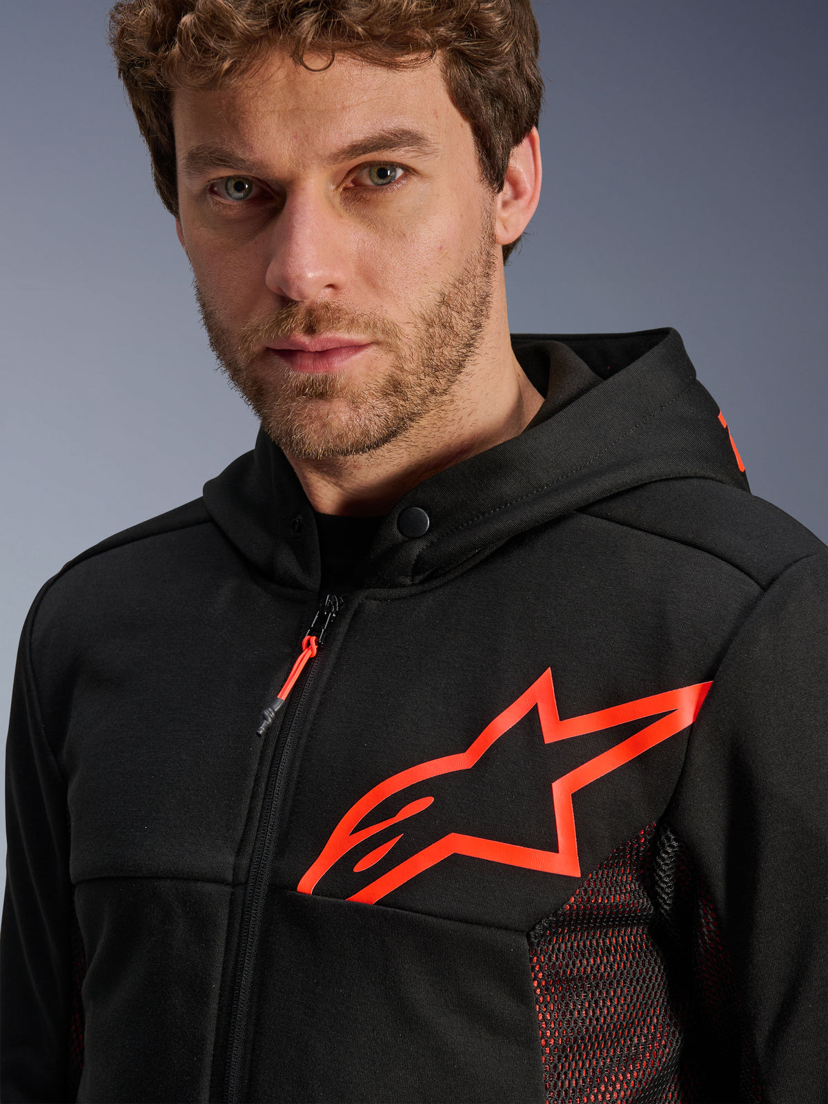 Alpinestars Chrome Air Sport Hoodie, zwart met fluo rood, close-up van het grote fluo rode sterlogo op de borst, rode mesh zijpanelen voor ventilatie, rits aan de voorzijde en kraag met drukknoop, casual urban motorkleding