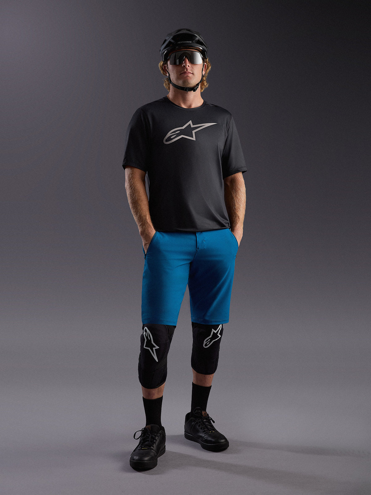 Alpinestars A-Dura Ride SS jersey en blauwe shorts, complete mountainbike-outfit met kniebeschermers en helm.