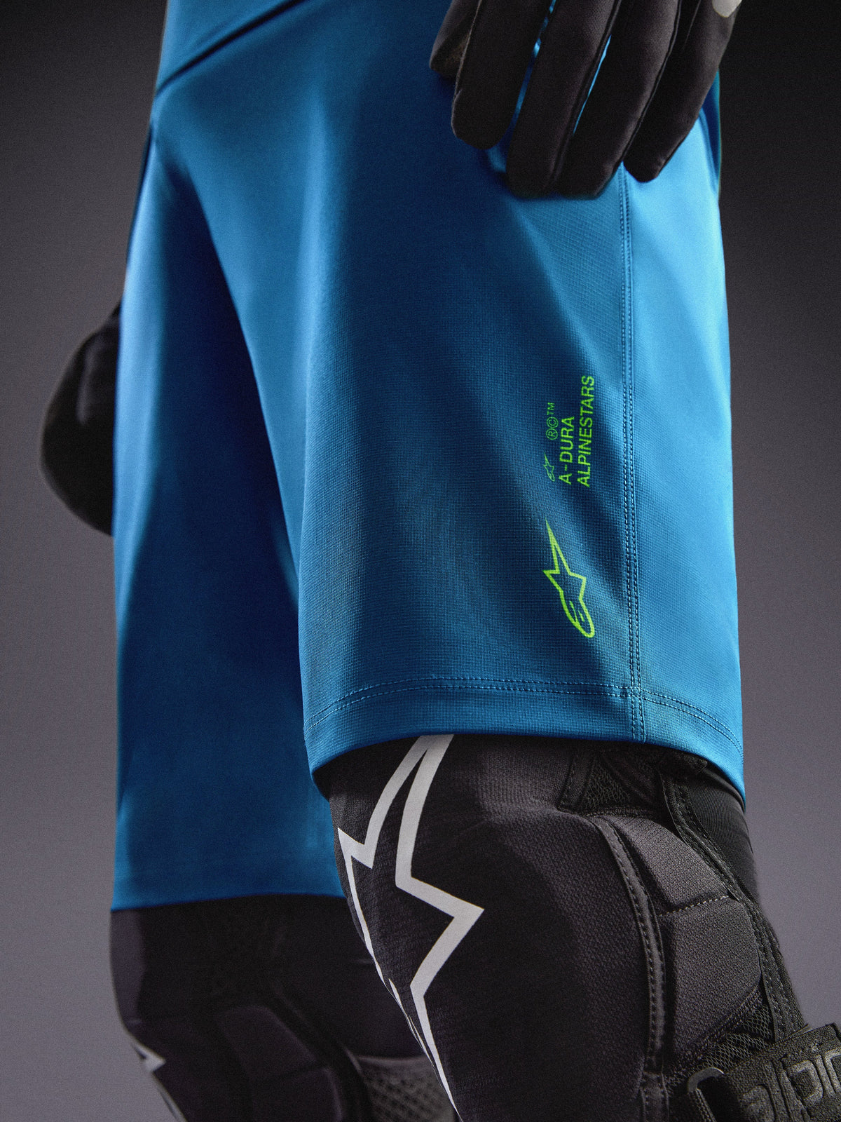 Alpinestars A-Dura Ride shorts in blauwgroen met limoengroene logo's, gecombineerd met kniebeschermers voor MTB.