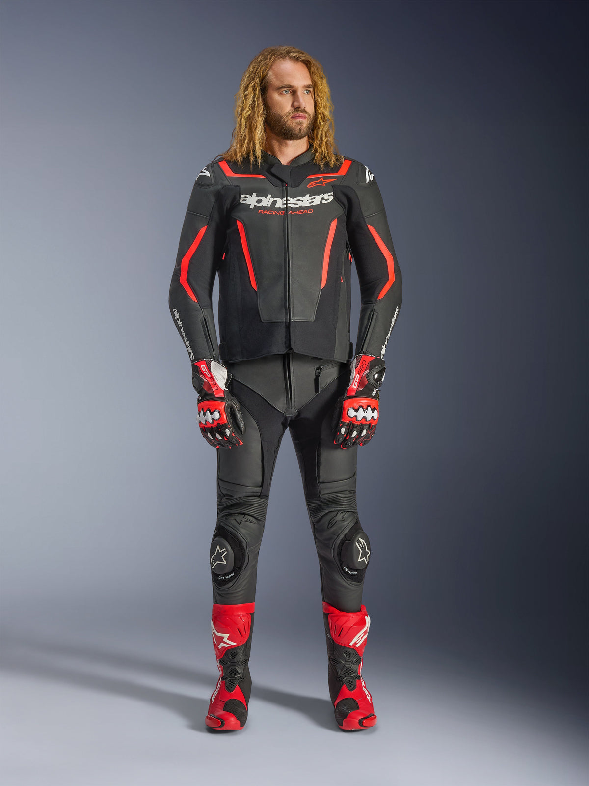 Male model wearing the Alpinestars GP Force V2 Leather Jacket in Black and Red Fluo, paired with matching leather pants, red racing gloves, and red performance boots, professional motorcycle sport gear