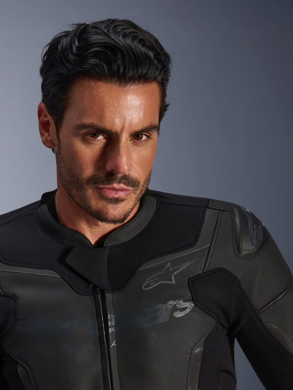 Close-up portret van een mannelijk model met het Alpinestars GP Force V2 lederen motorjack, zwart, vervaardigd uit hoogwaardig runderleer, met textiele stretchpanelen en een subtiel Alpinestars-sterritlogo, strak sportgericht ontwerp voor motorrijden op de weg.