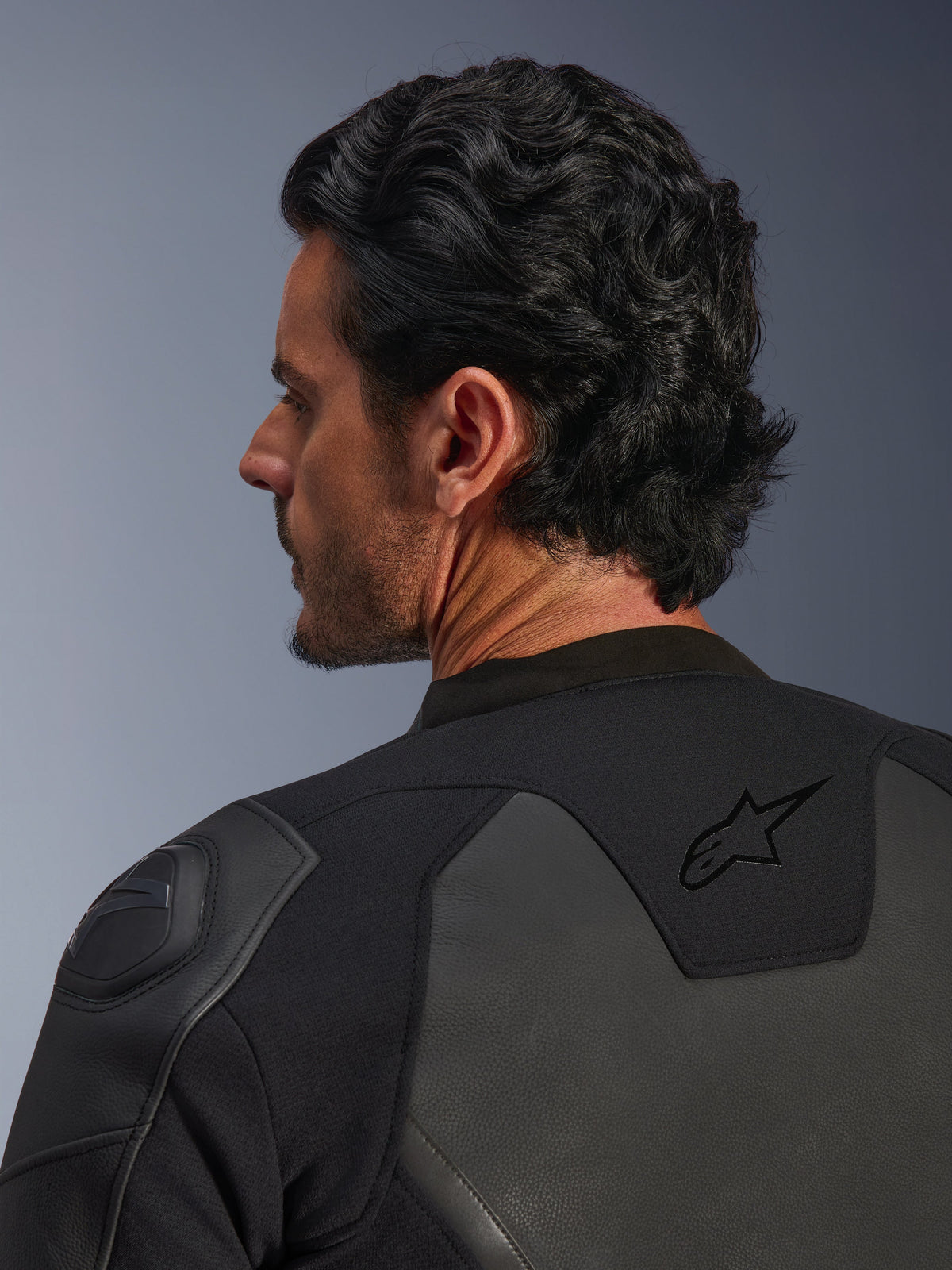 Alpinestars GP Force V2 leren jas, zwart, detailopname van achteren met het zwarte ster-logo op de bovenrug en GP Lite Evo DFS schouderbeschermer, meerpanelige constructie van leer en textiel, studio-opname van het profiel van de rijder en details van de uitrusting