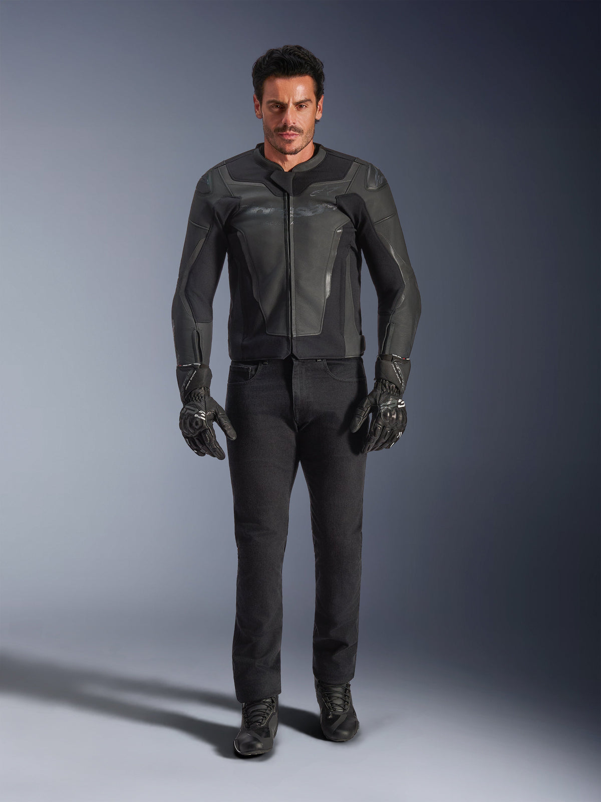 Alpinestars GP Force V2 leren jas in het zwart, gedragen door een mannelijke rijder met zwarte motorbroek, handschoenen en laarzen, slanke leren constructie in sportstijl met schoudersliders en geïntegreerde bescherming.