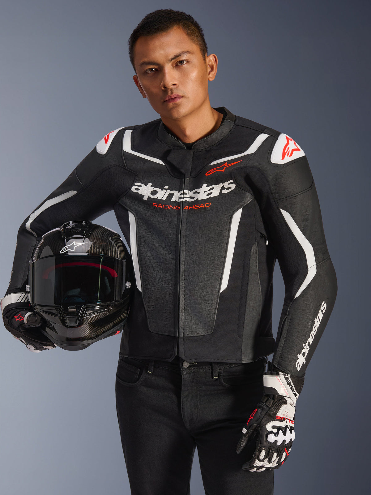 Alpinestars GP Force V2 leren jas, zwart en wit met rode accenten, gedragen door een model met een carbon motorhelm en racehandschoenen, voorzien van witte contrastpanelen en Alpinestars-branding.