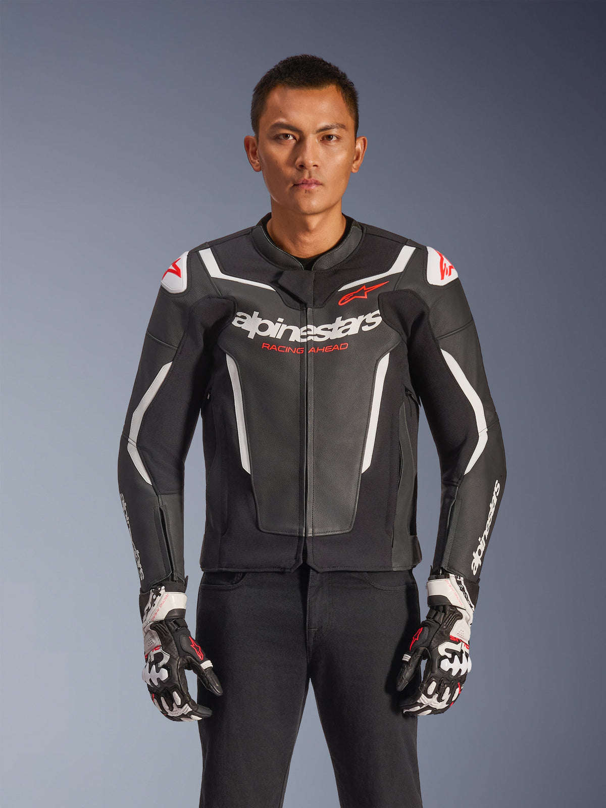 Alpinestars GP Force V2 leren jas, motorracejas, zwart en wit met rode accenten, premium lederen constructie met beschermende protectie, Racing Ahead-branding, gedragen met bijpassende handschoenen