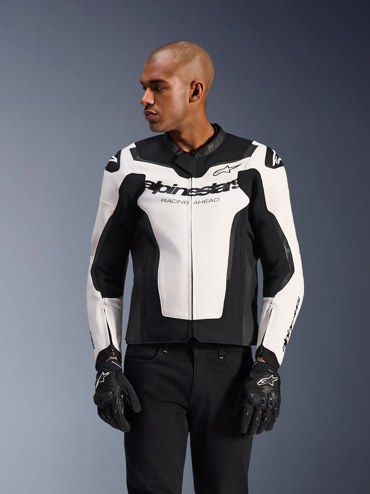 Alpinestars GP Force V2 Leather Jacket, White and Black, worn by a model with black motorcycle gloves and pants, featuring a bold color-blocked design with Alpinestars "Racing Ahead" branding on the chest, high-performance leather motorcycle gear