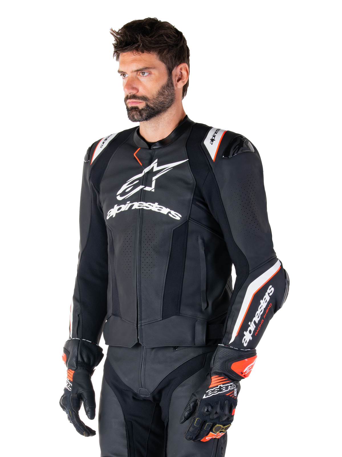 Male model wearing the Alpinestars Missile V3 Ignition Leather Jacket, Black with White and Orange accents, featuring prominent white logos, perforated leather sections, and protective shoulder armor, styled with racing gloves for a sport-racing look.