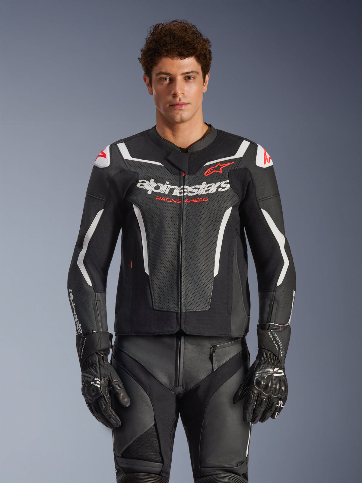 Alpinestars GP Force V2 Air Leather Jacket, Black with White and Red accents, model wearing perforated leather jacket with 'alpinestars' and 'RACING AHEAD' branding on the chest, paired with matching racing pants and gloves, premium sport motorcycle gear