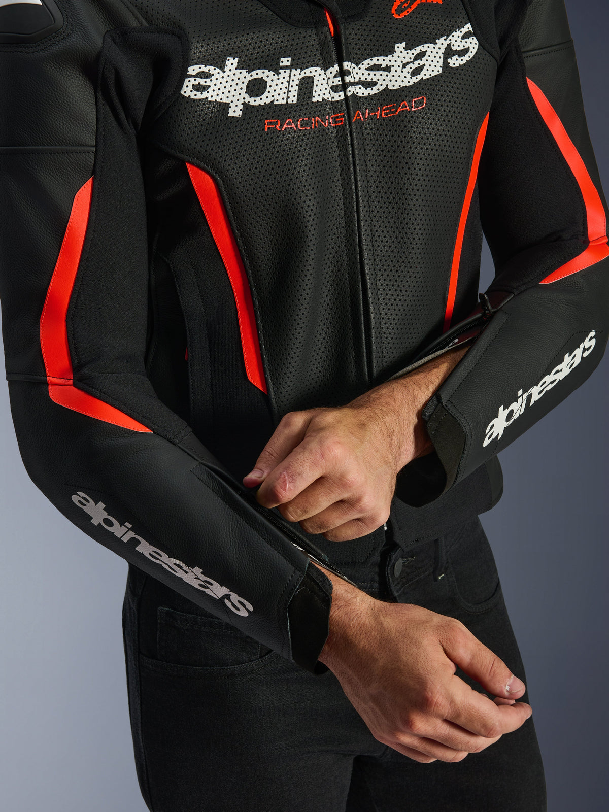 Alpinestars GP Force V2 Air Leather Jacket in Black and Red Fluo, close-up showing perforated leather construction, white branding on chest and sleeves, and a rider adjusting the forearm zipper for a tailored fit.
