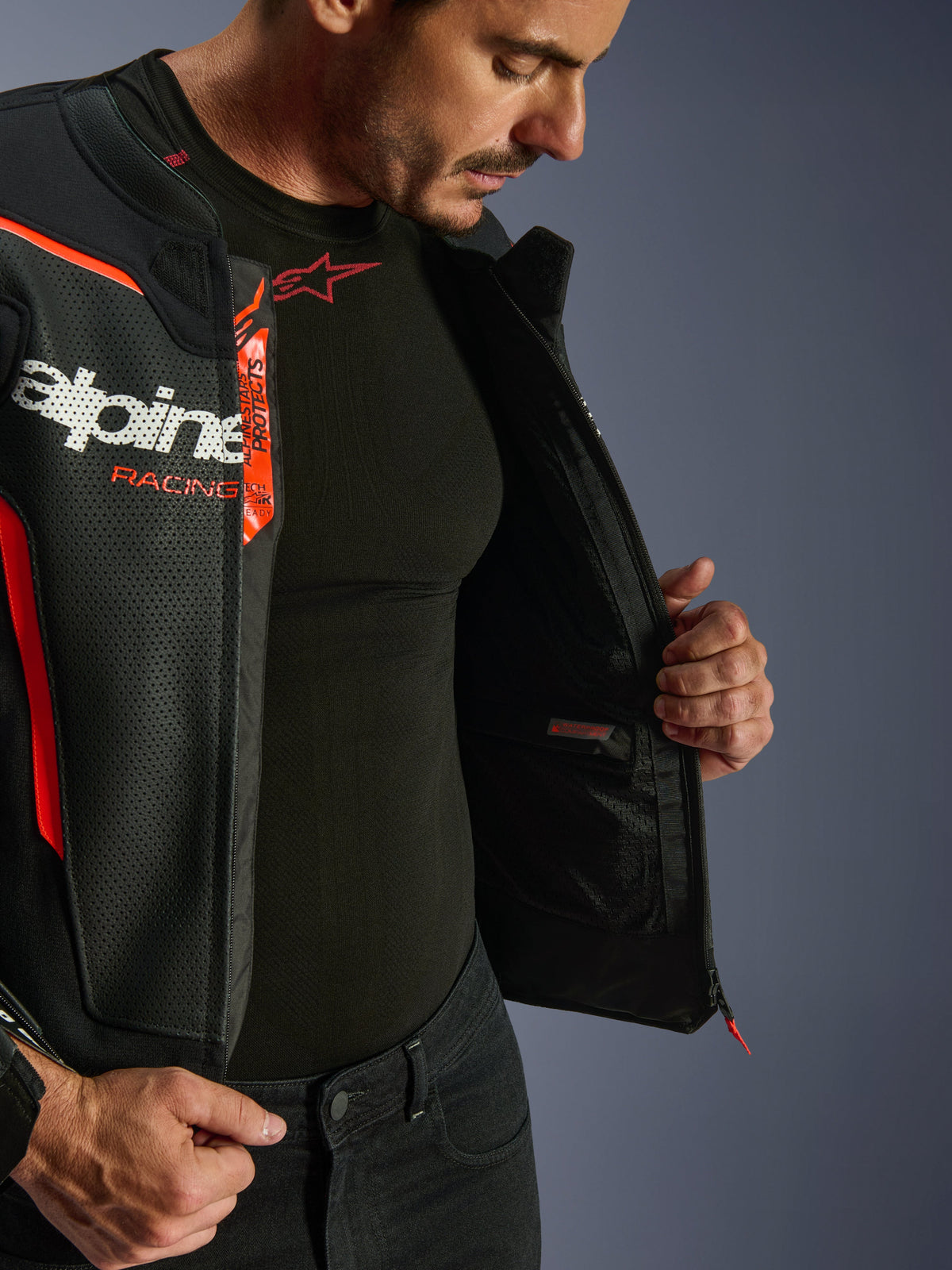 Alpinestars GP Force V2 Air Leather Jacket, Black and Red Fluo, unzipped to reveal internal waterproof pocket and branding, perforated leather multi-panel construction for airflow, worn with black Alpinestars base layer
