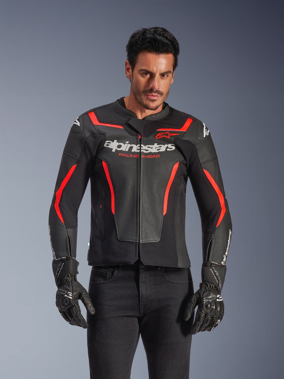 Alpinestars GP Force V2 Air Leather Jacket, Motorcycle Racing Jacket, Black and Red Fluo, premium leather construction with extensive perforations for airflow, worn by a model with black gloves and pants, featuring bold branding and 'Racing Ahead' text on the chest