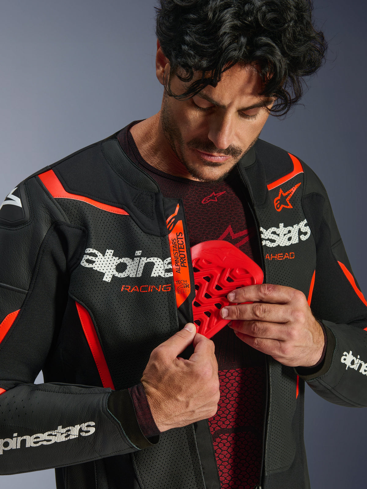 Alpinestars GP Force V2 Air Leather Jacket in Black and Red Fluo, man unzipping the jacket to reveal a red chest protector being inserted, featuring perforated leather, bold white branding, and Tech-Air Ready detail on the internal flap