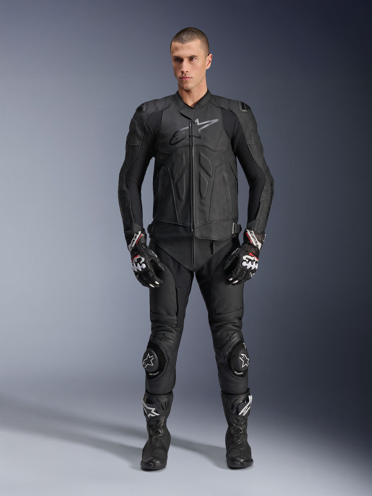 Alpinestars Dusk Leren Jas, zwart, gedragen door een mannelijk model als onderdeel van een complete race-geïnspireerde outfit met bijpassende leren broek, handschoenen en laarzen, strak ergonomisch ontwerp met bescherming op de schouders en logo op de borst