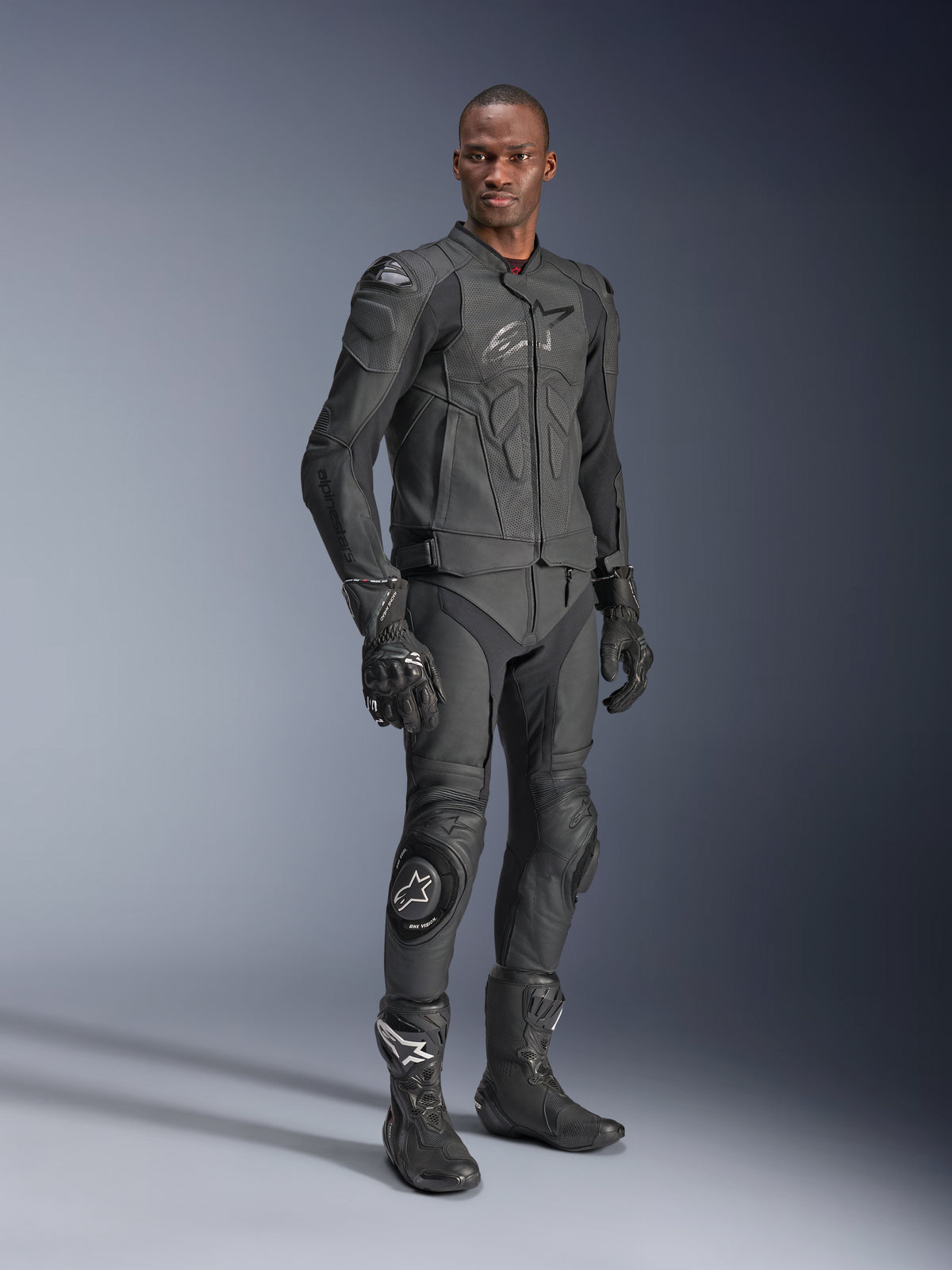 Alpinestars Dusk Airflow Leren Jas, Black Black, gedragen door een motorrijder in volledige technische uitrusting inclusief bijpassende leren broek, handschoenen en laarzen, voorzien van geperforeerde leren panelen voor ventilatie en geïntegreerde bescherming voor sportief motorrijden