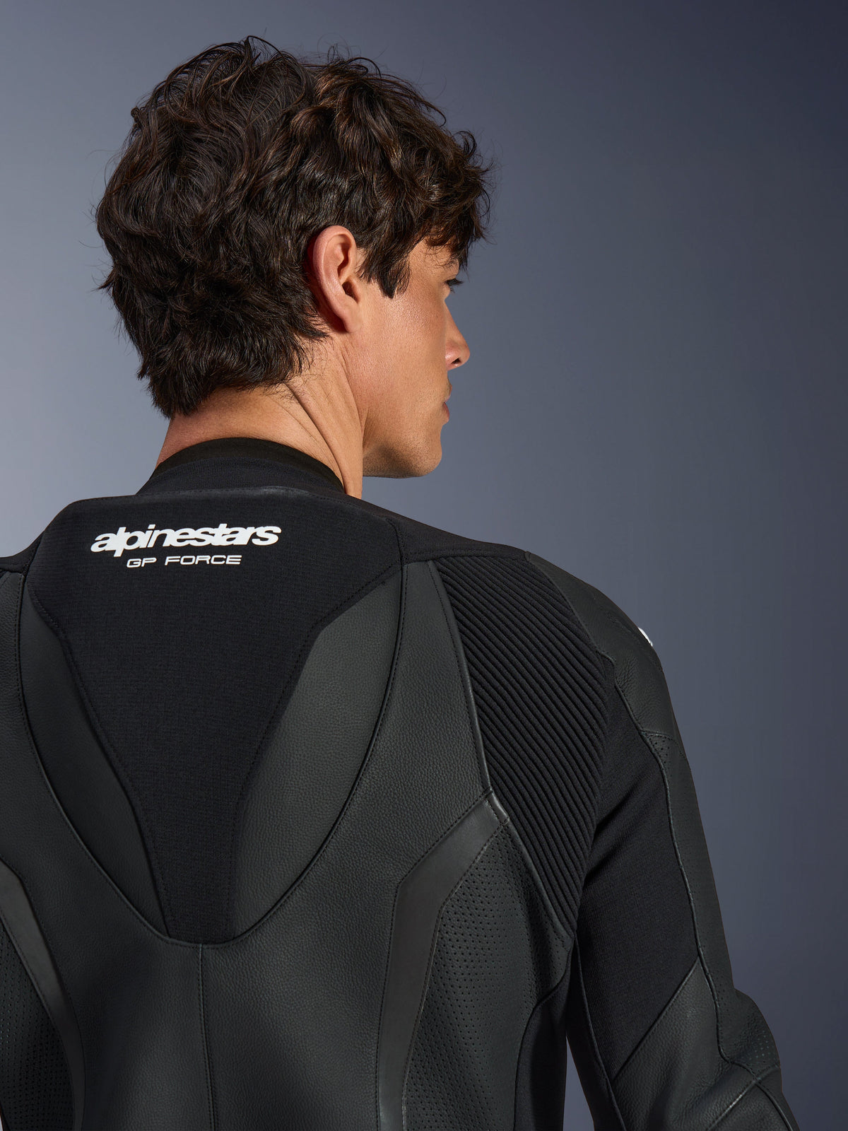 Alpinestars GP Force V2 Leren Pak 1-delig, zwart, detailopname van de bovenrug en aerodynamische speedhump, met witte branding, geperforeerde leren secties en accordeon stretchpanelen voor raceprestaties.