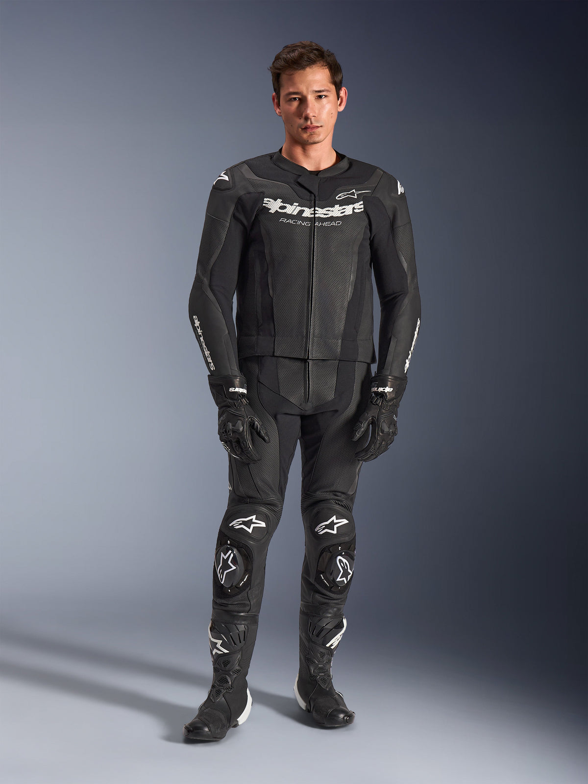 Alpinestars GP Force V2 tweedelig leren pak, zwart met witte logo's, volledig motorracepak, hoogwaardige leren constructie met verstevigde kniesliders en geperforeerde panelen, gedragen met zwarte handschoenen en laarzen, studio-opname in volledige lengte