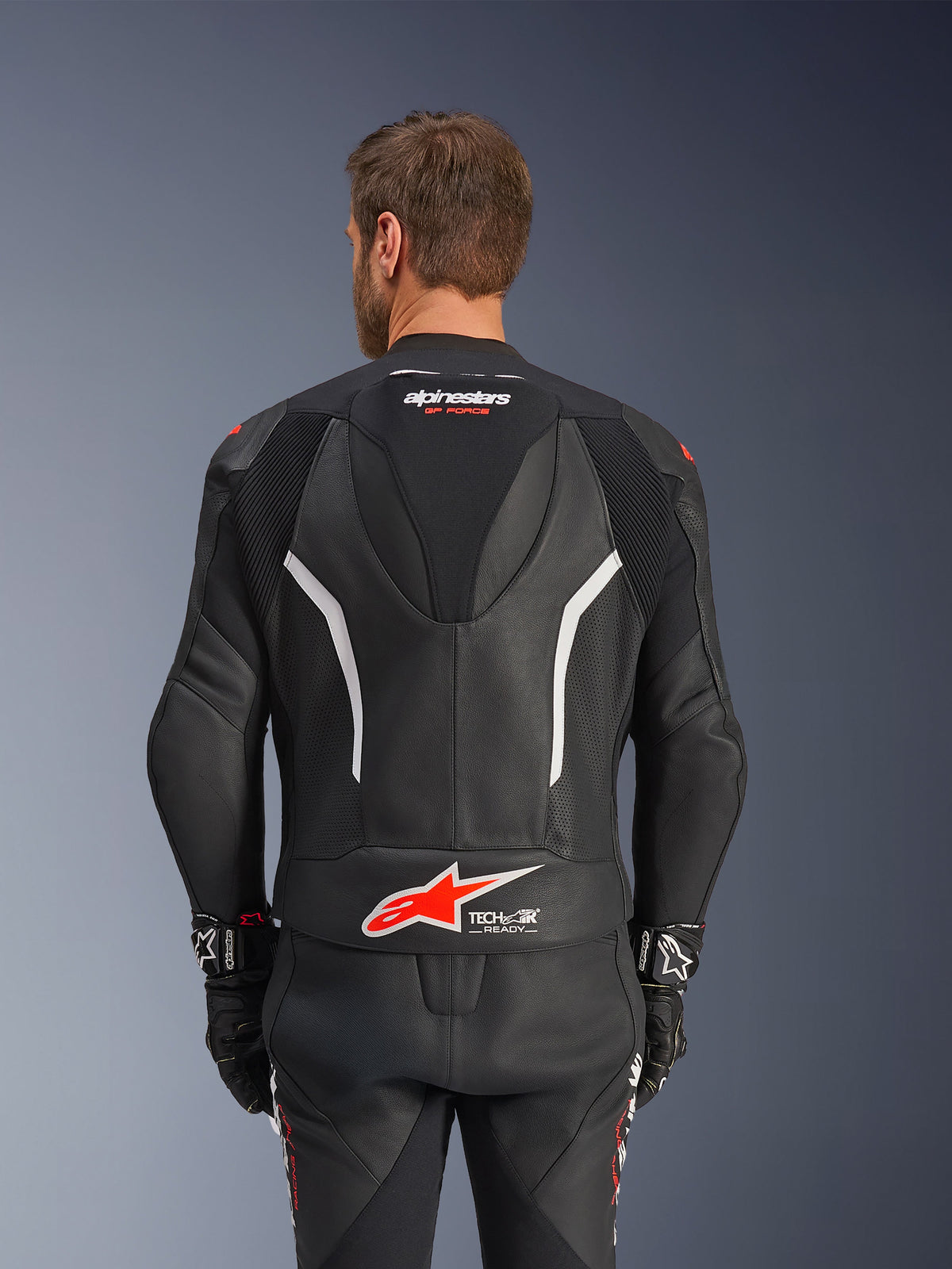 Alpinestars GP Force V2 tweedelig leren pak, zwart, wit en rood fluo, achteraanzicht van het leren jack, voorzien van het Tech-Air Ready logo, witte accenten, geperforeerde lederen panelen en accordeonstretch voor bewegingsvrijheid.