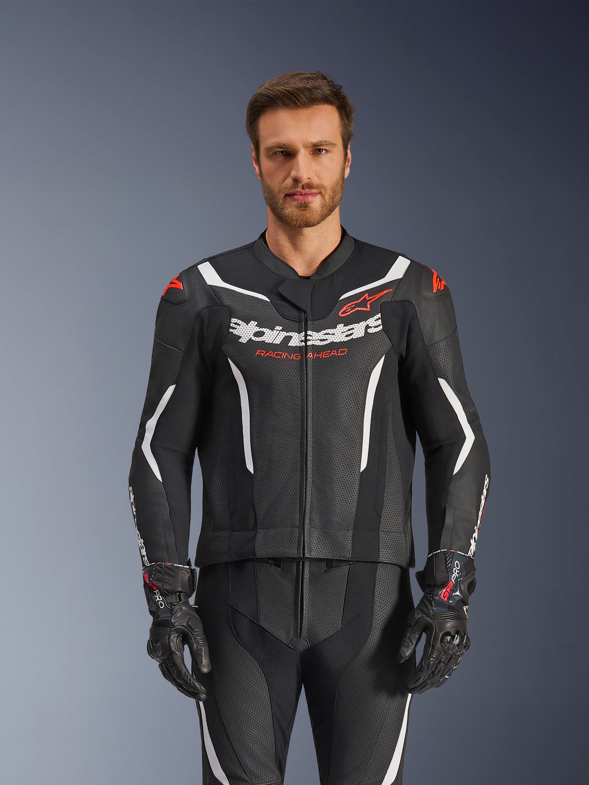 Alpinestars GP Force V2 lederen pak - 2-delig, zwart, wit en fluo rood, vooraanzicht van een mannelijk model dat het geperforeerde lederen pak draagt met bijpassende zwarte handschoenen, met witte hoekige accenten en Alpinestars-branding op de borst