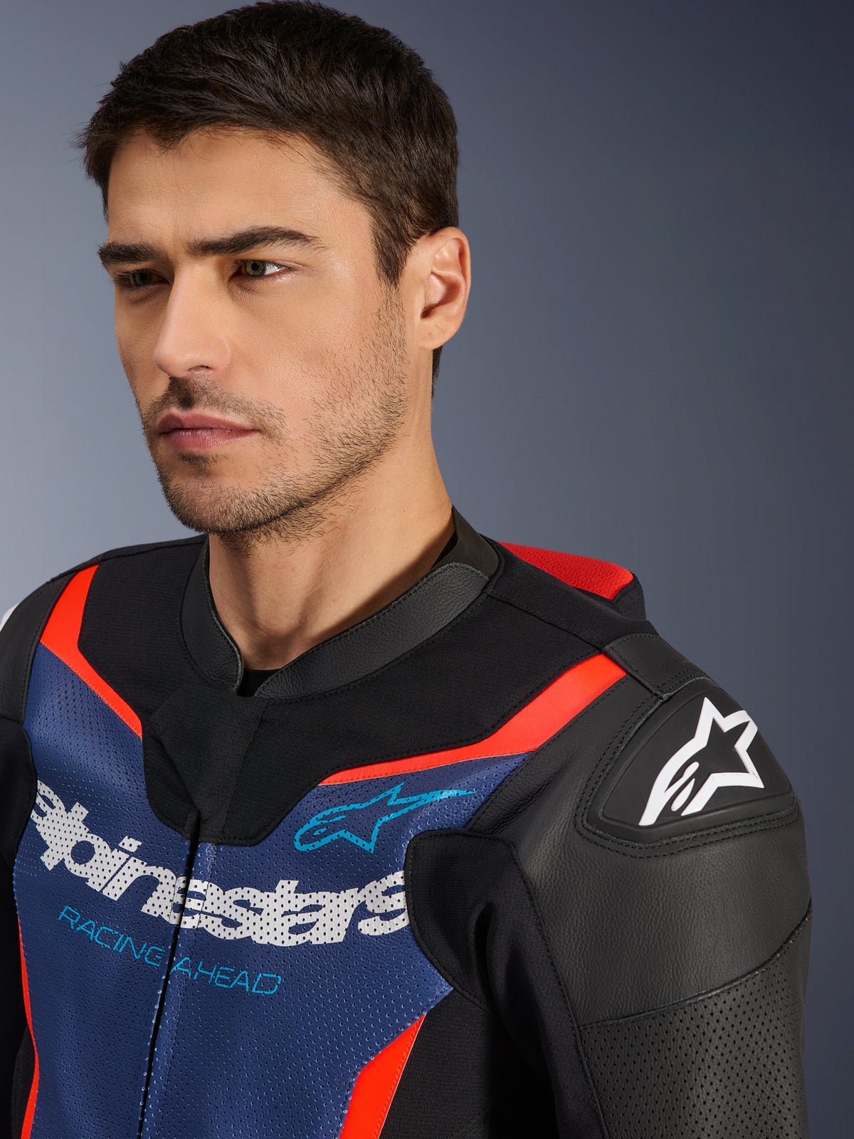 Alpinestars GP Force V2 Leren Pak 2-delig, zwart, blauw en fluo rood, close-up van een model dat het motorjack draagt, met geperforeerde runderlederen panelen, Alpinestars-logo op de schouder en 'Racing Ahead' branding op de borst, professionele race-uitrusting