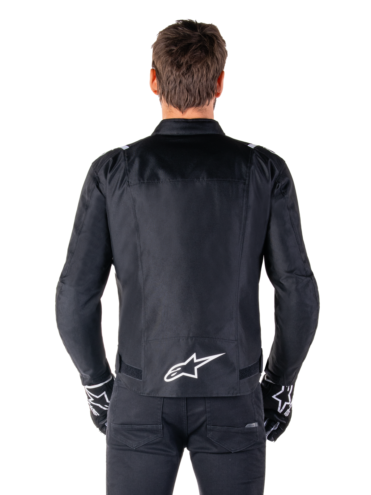 Alpinestars T-SPS V2 Waterproof Jacket, zwart en wit, rugaanzicht met wit Alpinestars-logo op de onderrug, gedragen met zwarte broek en handschoenen, sportief gesneden textiele motorjas