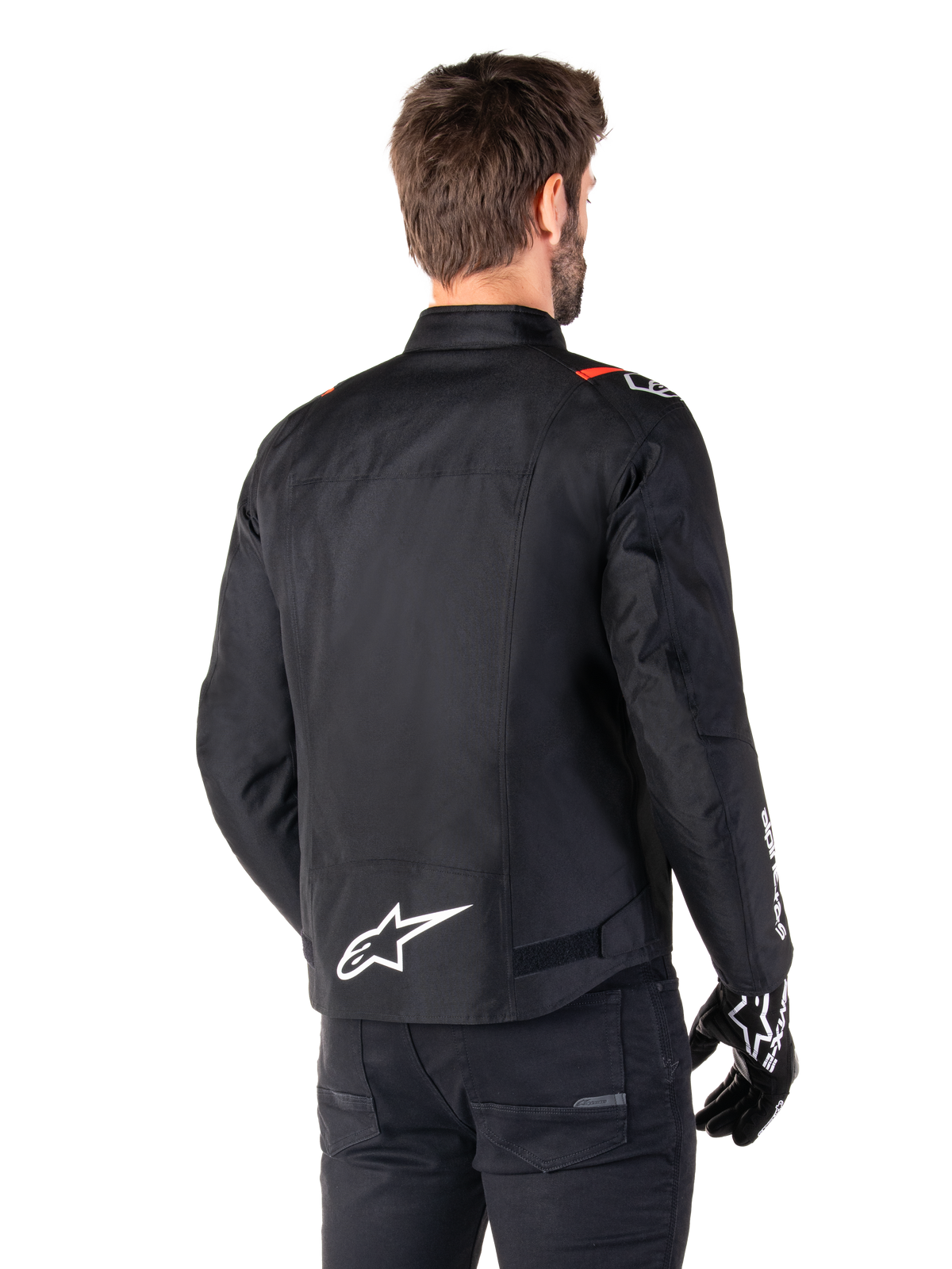 Alpinestars T-SPS V2 Waterproof Jas, Zwart Wit Rood Fluo, achteraanzicht, met wit Alpinestars-logo op de onderrug en rode accenten op de schouders, gedragen met zwarte motorhandschoenen en broek, sportieve textiele motorjas