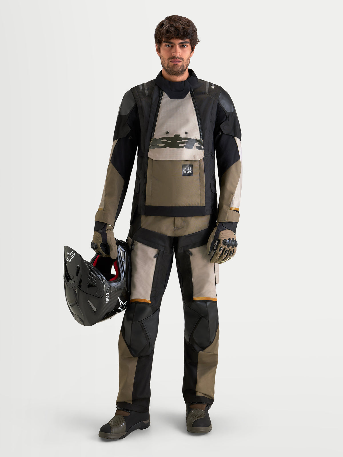Alpinestars Harok V2 Drystar jas, heren adventure motorjas in aluminium, bruin en zwart, gedragen met bijpassende adventure-uitrusting terwijl hij een helm vasthoudt