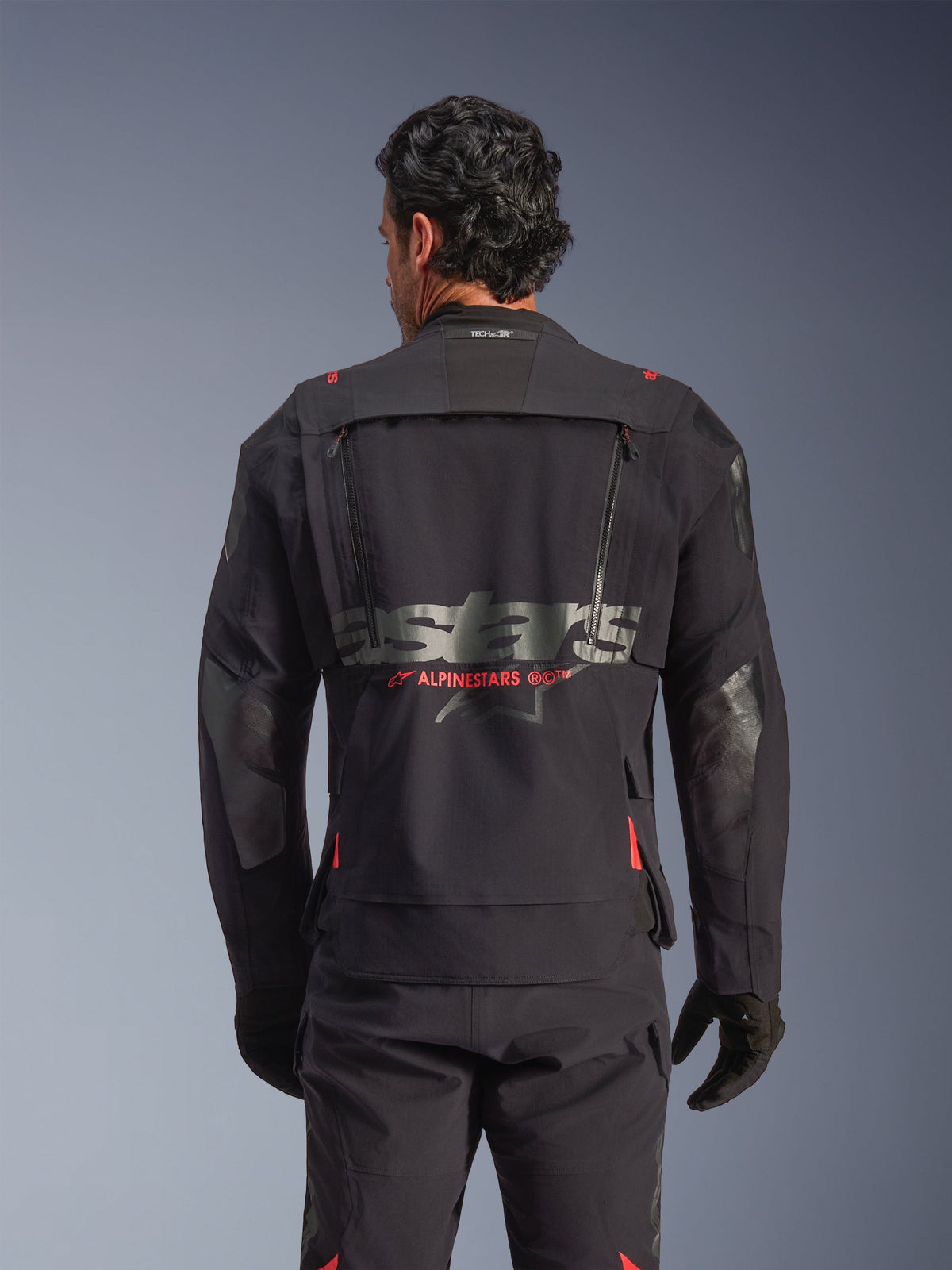Alpinestars Halo Pro Drystar® XF Gelamineerd Jack in Black Dark Shadow, achteraanzicht op model, technisch ventilatiepaneel op de rug met ritsen, rode Alpinestars logo-accenten, Tech-Air® branding in de nek, modulaire adventure motorjas.