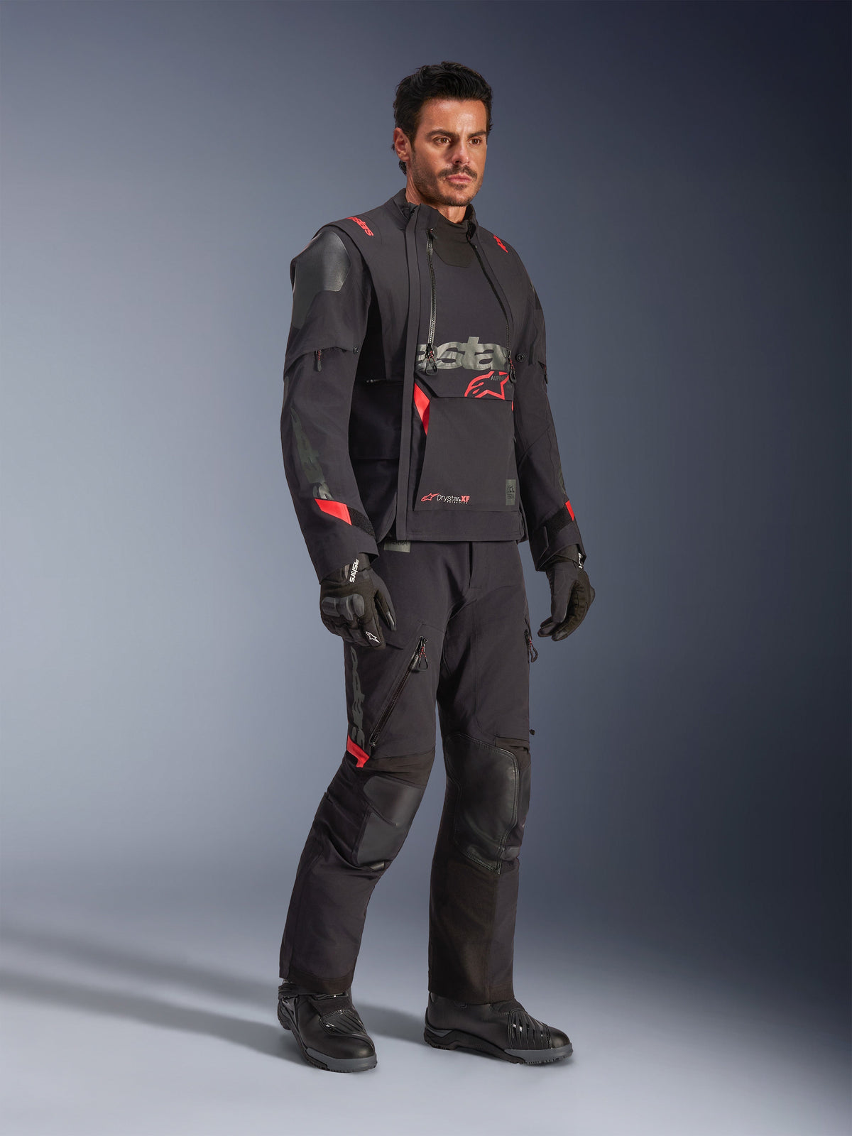 Male rider wearing the Alpinestars Halo Pro Drystar® XF Laminated Jacket in Black Dark Shadow, complete adventure riding gear with matching pants, gloves, and boots, featuring modular asymmetrical front panels and red branding accents.