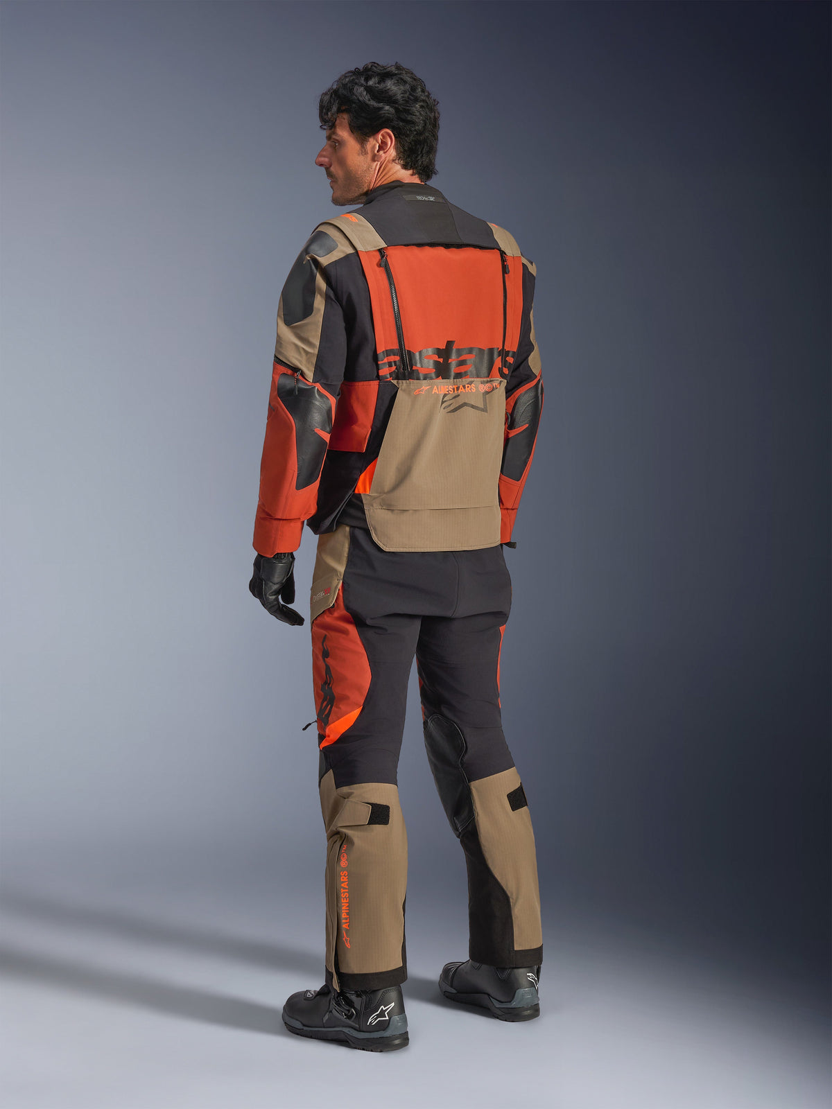Alpinestars Halo Pro Drystar® XF gelamineerd jack, Walnut Rust Black adventure motorjas, achteraanzicht gedragen met bijpassende broek en zwarte laarzen, voorzien van technisch 3L-stretchmateriaal, modulaire ventilatiepanelen en oranje branding op de achterzijde