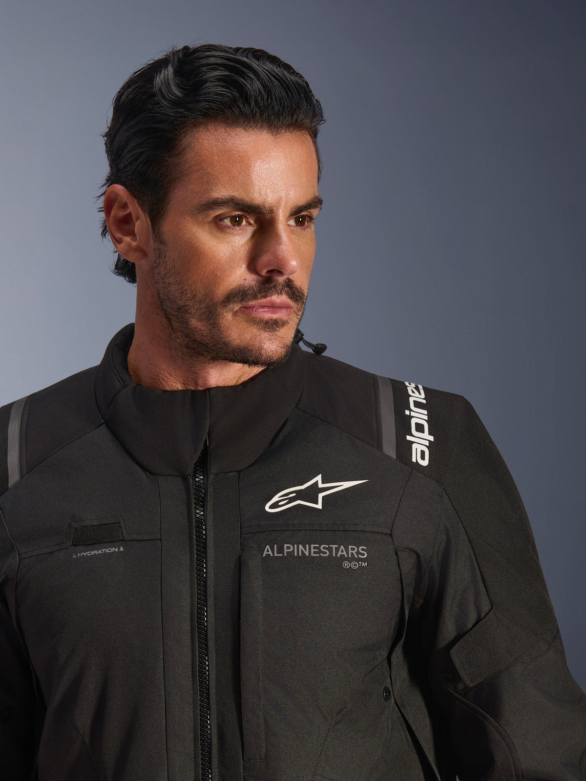 Alpinestars Andes V4 Drystar® jas, zwart, gedragen door een mannelijk model, close-up opname van de borst en schouders, voorzien van witte Alpinestars-logo's, textielmateriaal met ventilatiedetails en lus voor hydratatieslang, adventure-touring motorkleding