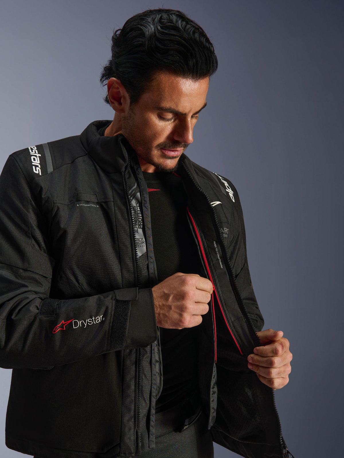 Alpinestars Andes V4 Drystar® Jacket, zwarte adventure motorjas, man demonstreert de interne thermische voering en rode rits, voorzien van Drystar®-branding op de mouw, duurzaam textielmateriaal voor rijden in alle weersomstandigheden