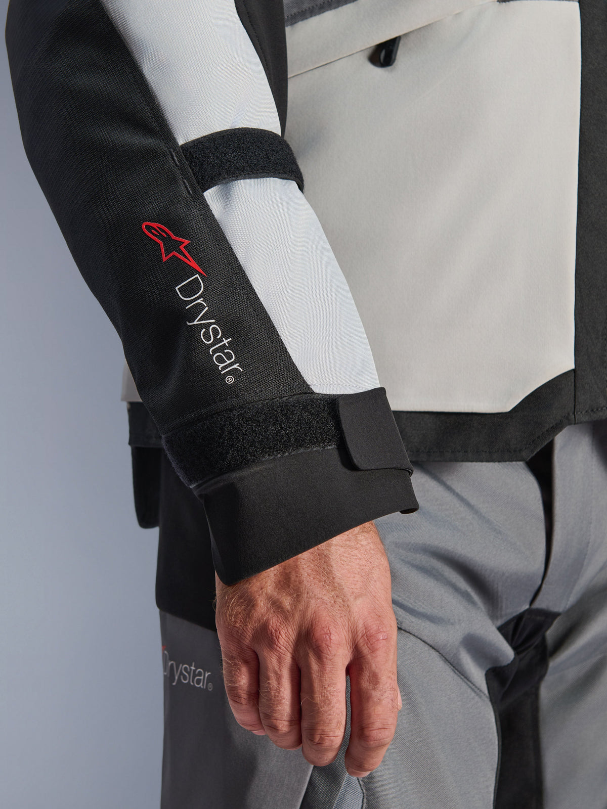 Alpinestars Andes V4 Drystar® Jas, adventure motorjas, Ice Gray en zwarte panelen, close-up van de mouw met rood Drystar® logo en verstelbare bandjes, functioneel textielontwerp voor rijden in alle weersomstandigheden