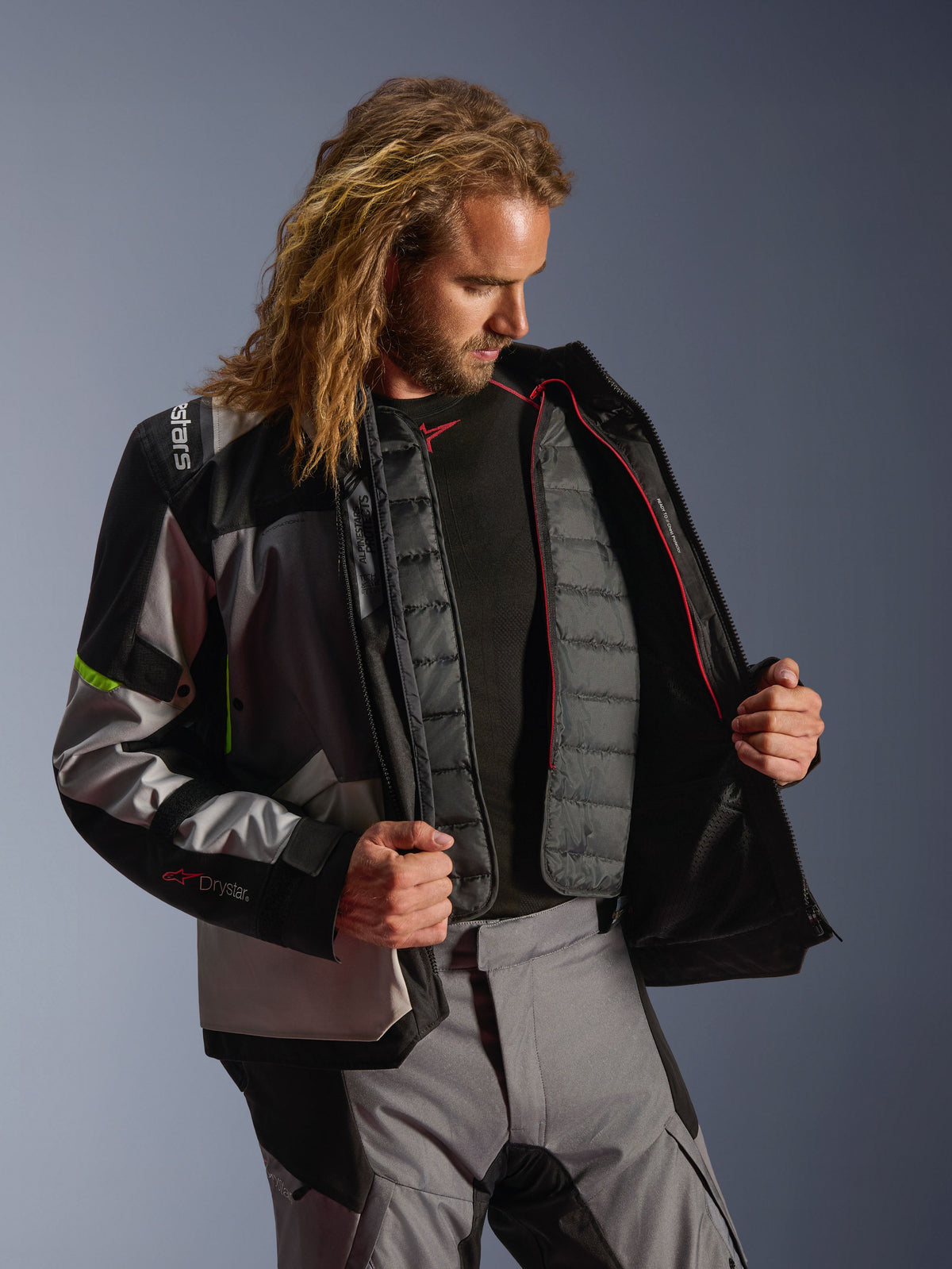 Alpinestars Andes V4 Drystar® Jas, adventure motoruitrusting in Dark Gray, Ice Gray en Yellow Fluo, mannelijk model toont de interne gewatteerde thermische voering, gedragen met bijpassende motorbroek, ontwerp voor prestaties in alle weersomstandigheden