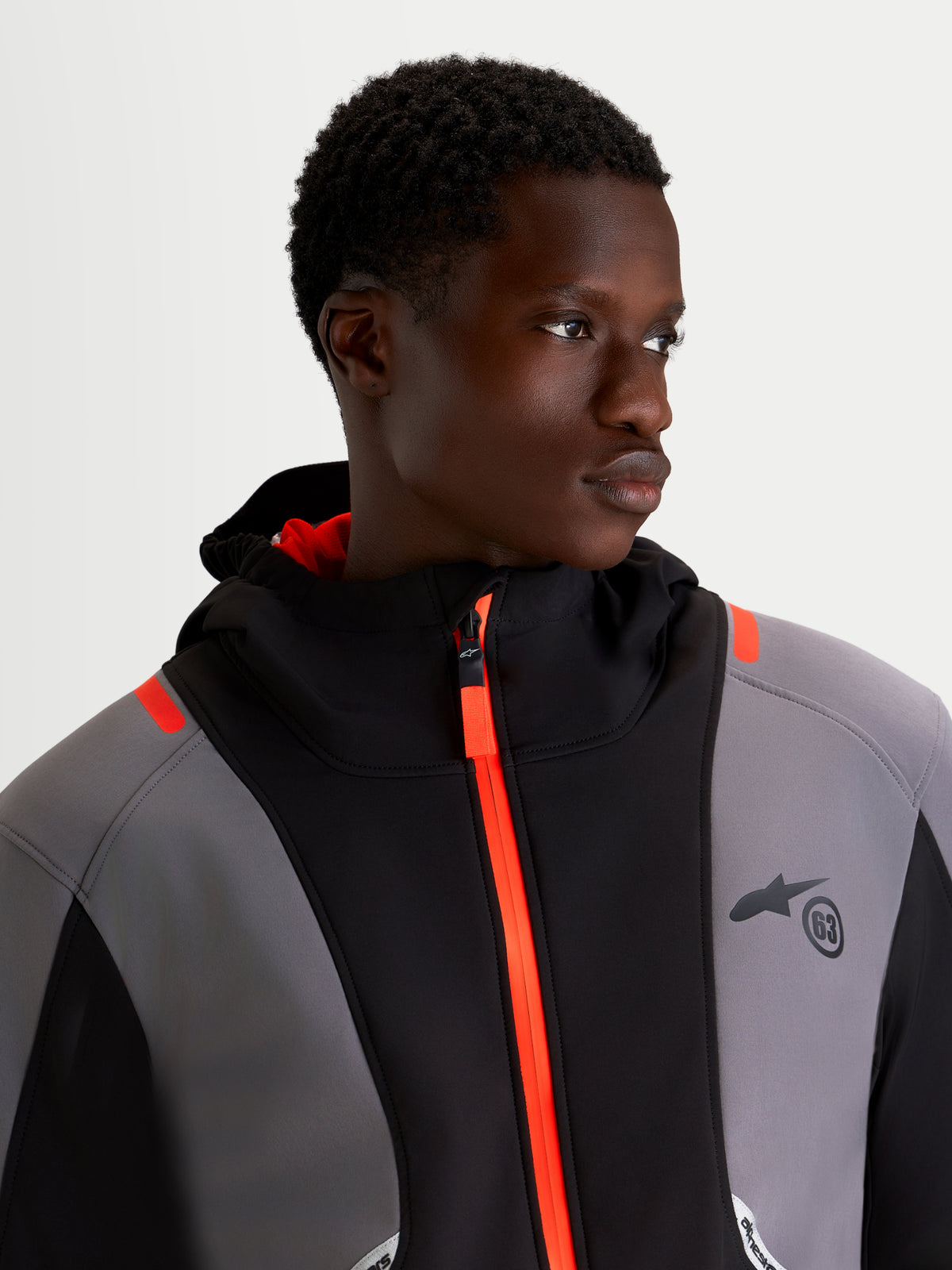 Alpinestars C 5 Drystar jas, heren motorjas voor urban rijden in zwart en donkergrijs, close-up van model met de waterdichte softshell jas met helderoranje ritssluiting en geïntegreerde capuchon