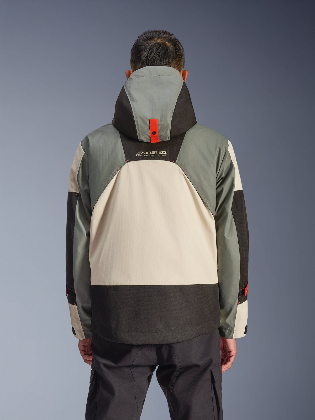 Achteraanzicht van de Alpinestars Mospher Waterproof Jacket in Fur Gray Black Ice, met een meerkleurig grijs, crème en zwart paneelontwerp, parka-silhouet met capuchon en rood drukknopdetail voor de verankering, 'MO.ST.EQ.'-branding, gecombineerd met een zwarte cargo motorbroek