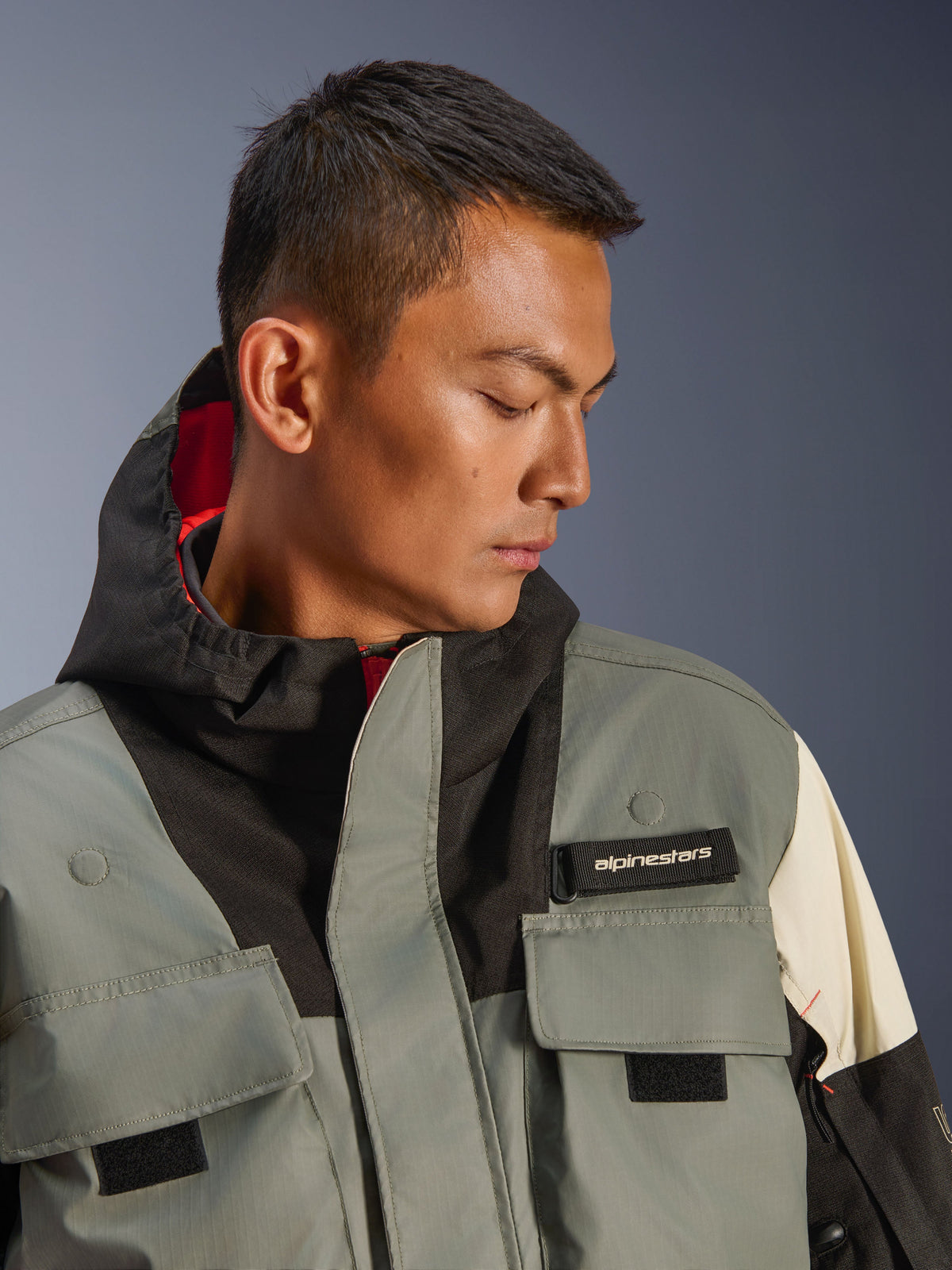 Alpinestars Mospher WP Jacket, waterdichte motorparka, Fur Gray Black Ice, close-up van model dat jas met capuchon draagt met functionele zakken, zwart Alpinestars-logolabel en tactisch ontwerp met rode binnenvoering