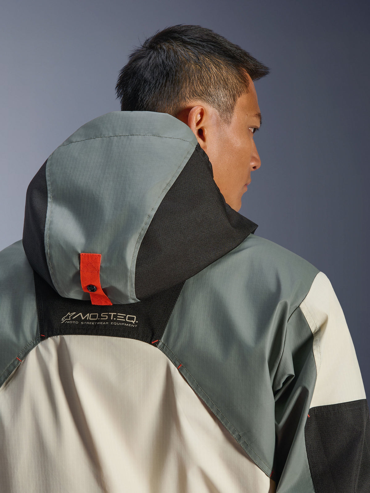 Alpinestars Mospher Waterproof Jacket, Fur Gray Black Ice, close-up achteraanzicht van het capuchonverankeringssysteem met een oranje drukknooplipje, MO.ST.EQ. Moto Streetwear Equipment-branding, duurzame ripstop textielconstructie