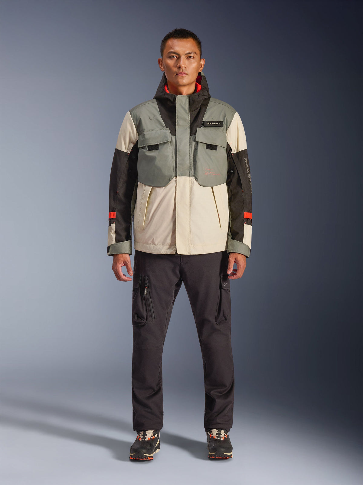 Alpinestars Mospher Waterproof Jacket in Fur Gray Black Ice, motorparka in tactische stijl gedragen door een mannelijk model met een donkere cargobroek, ontwerp met meerdere zakken en kleurvlakken in grijs, crème en zwart, urban commuter motorkleding