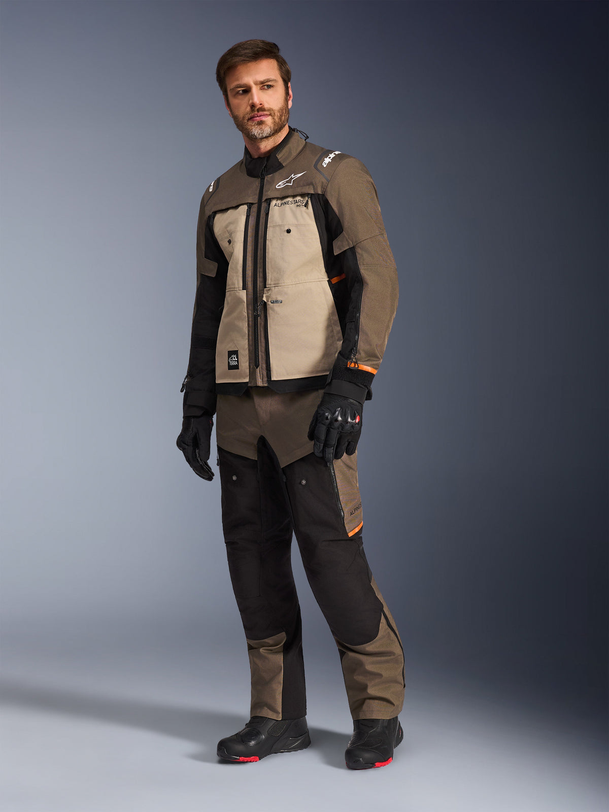 Alpinestars Cusco Drystar® Jacket in Walnut Aluminum Black, worn by a male model with matching motorcycle pants and gloves, adventure-touring design featuring tan chest panels and black accents.