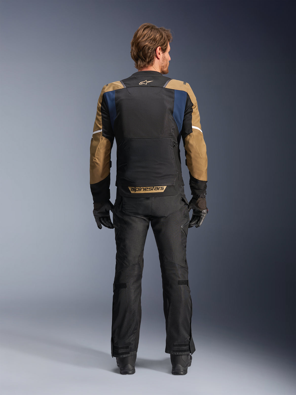 Alpinestars ST-2 Air Jas in Deep Blue, Dark Khaki en Black, achteraanzicht op model met een groot mesh rugpaneel en khaki mouwen met witte strepen, gecombineerd met een zwarte technische motorbroek en handschoenen voor adventure touring.