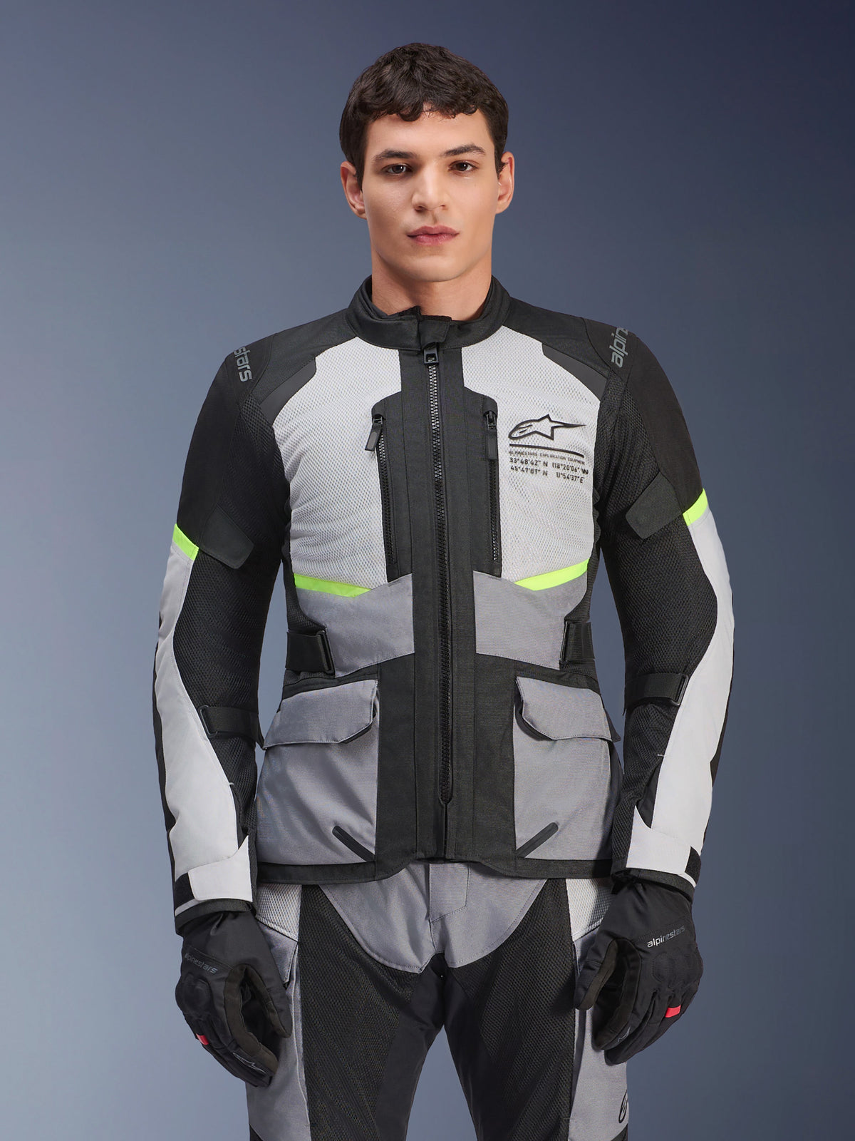 Mannelijke motorrijder in Alpinestars Andes Air Drystar® jas in Ice Gray, Dark Gray en zwart, voorzien van neongele accenten en mesh ventilatiepanelen, gecombineerd met bijpassende motorbroek en handschoenen, adventure touring uitrusting