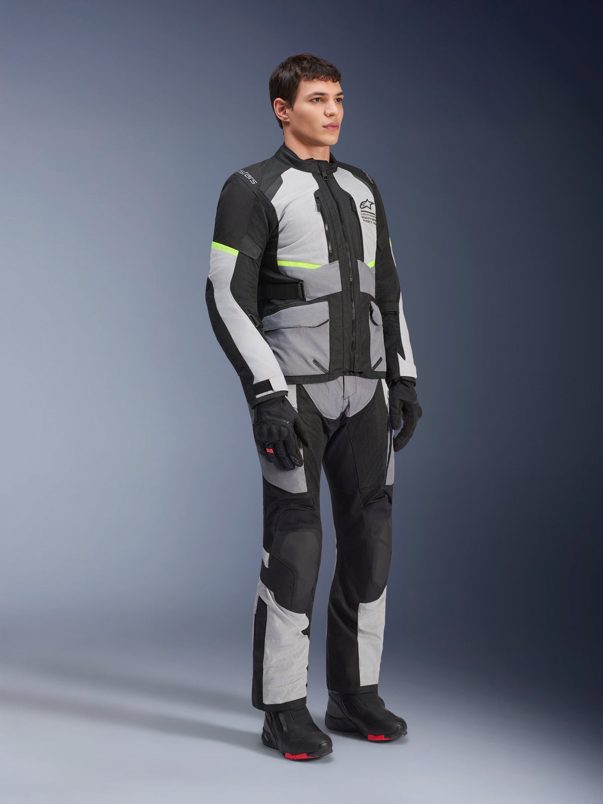 Alpinestars Andes Air Drystar® jas en broek, adventure touring motoruitrusting, Ice Gray, Dark Gray en zwart met neongele accenten, gedragen met zwarte handschoenen en laarzen, volledige studio-opname voor tweeseizoenen touring.