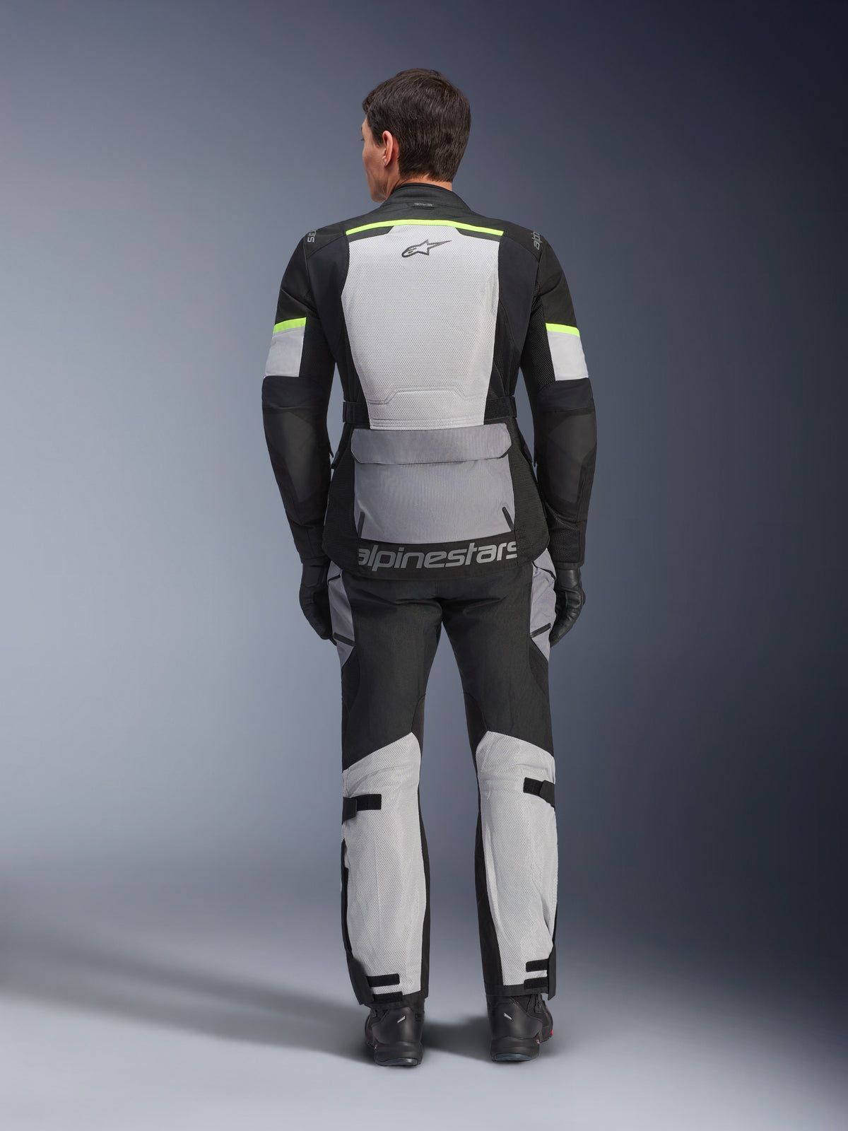 Alpinestars Andes Air Drystar® jas en broek, Ice Gray Dark Gray Black adventure touring set, achteraanzicht van rijder in complete uitrusting met neongele accenten, voorzien van grote mesh ventilatiepanelen en Alpinestars branding.