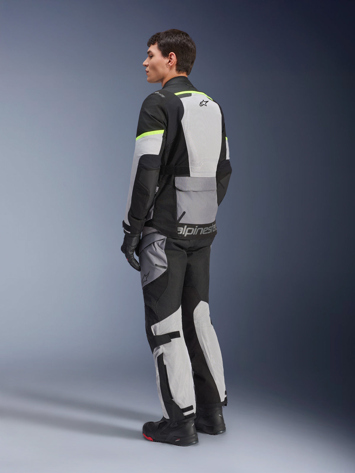 Alpinestars Andes Air Drystar® Jas, touring motorjas, Ice Gray en Dark Gray met zwarte panelen en neongele accenten, gedragen met bijpassende broek en handschoenen, driekwart achteraanzicht met mesh ventilatie en Alpinestars-branding.