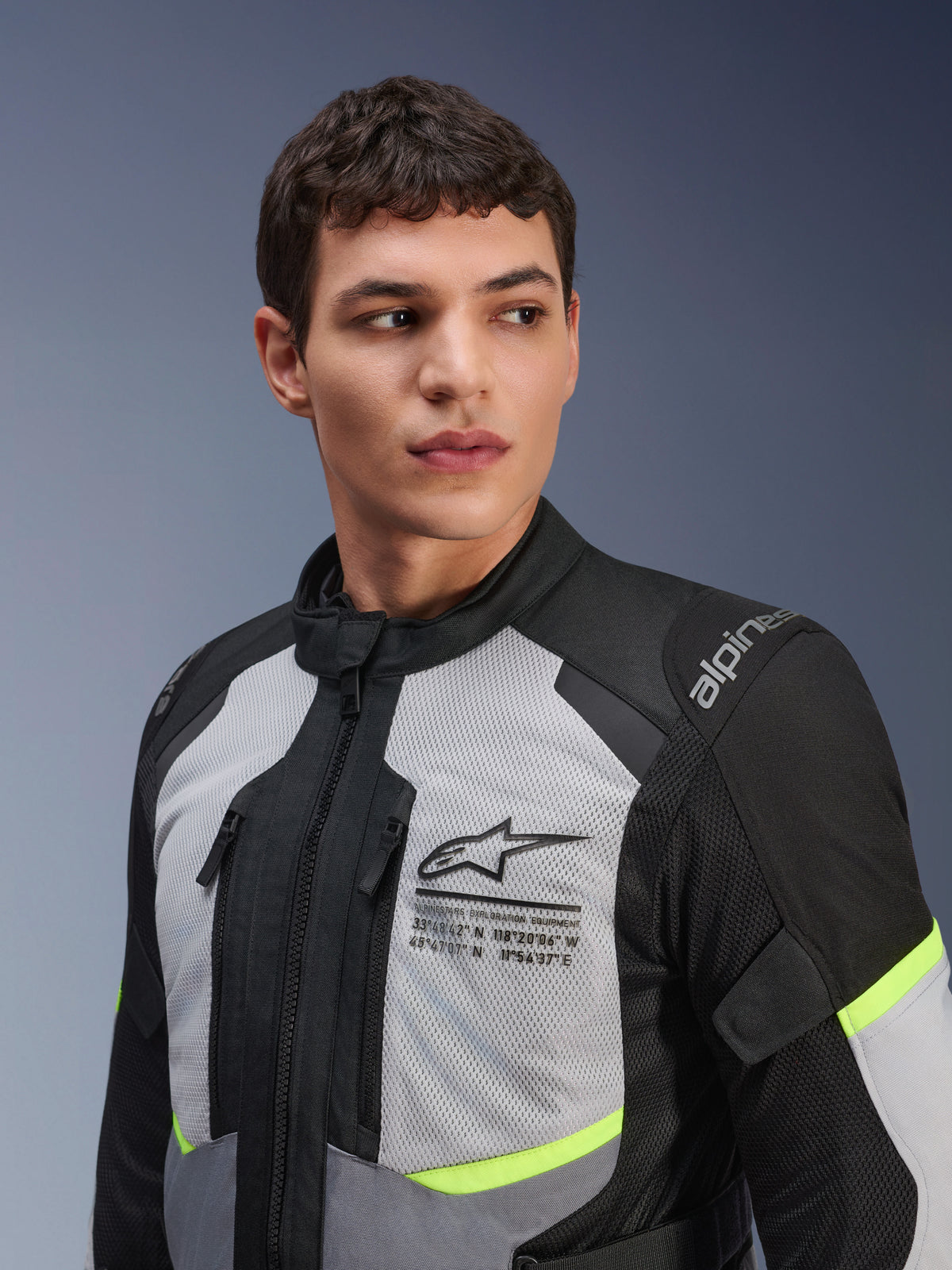 Alpinestars Andes Air Drystar® Jas, motor touringjas, Ice Grey en Dark Grey met neongele accenten, gedragen door een mannelijk model, voorzien van 2D-mesh panelen voor ventilatie, Alpinestars-logo met coördinaten op de borst, duurzame textielconstructie.
