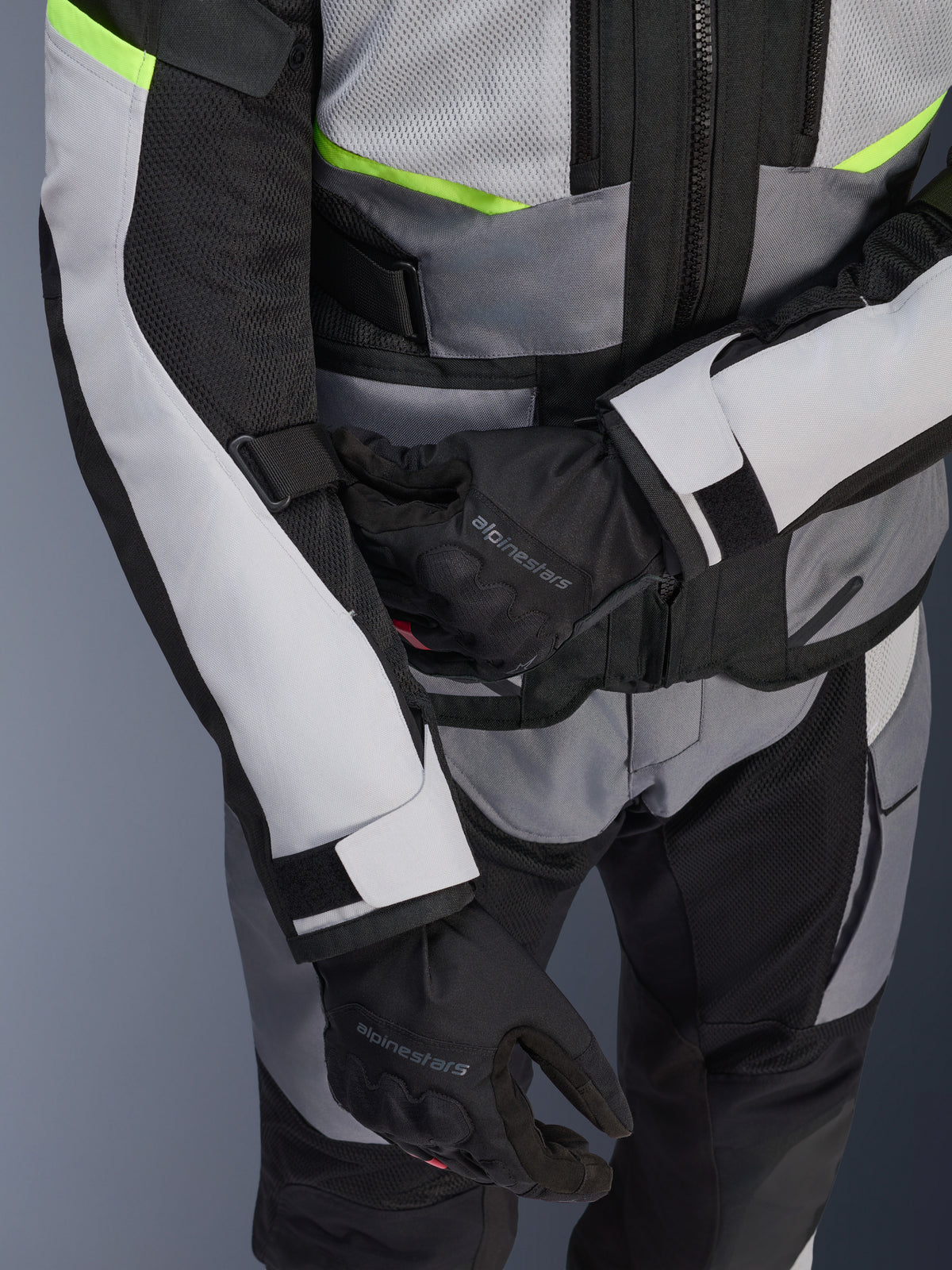 Alpinestars Andes Air Drystar® jas, motor-touringjas, ijsgrijs en donkergrijs met neongele accenten, close-up van meshpanelen en verstelbanden, gedragen met zwarte Alpinestars handschoenen