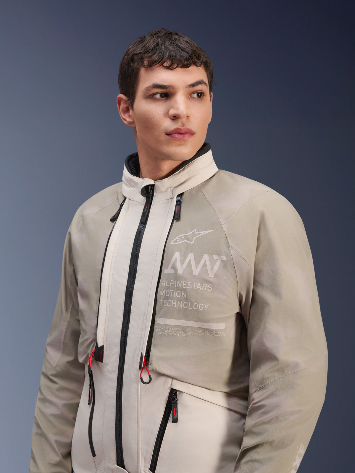 Alpinestars AMT-10LAB Drystar® XF Jas, White Sand Aluminum Camo, modulaire adventure motorjas, met "Alpinestars Motion Technology" branding op de borst, gedragen door een mannelijk model.