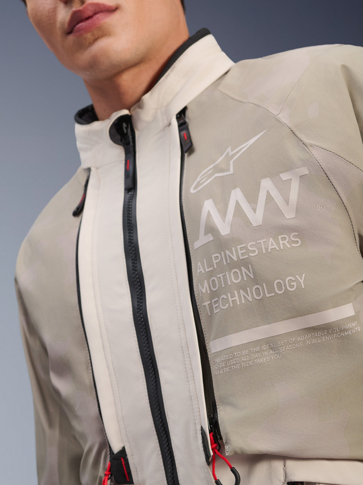 Alpinestars AMT-10LAB Drystar® XF Jas, White Sand Aluminum Camo, close-up van de borst met AMT Alpinestars Motion Technology branding, waterdichte ritsen met rode trekkers en getextureerd adventure-ready textiel.